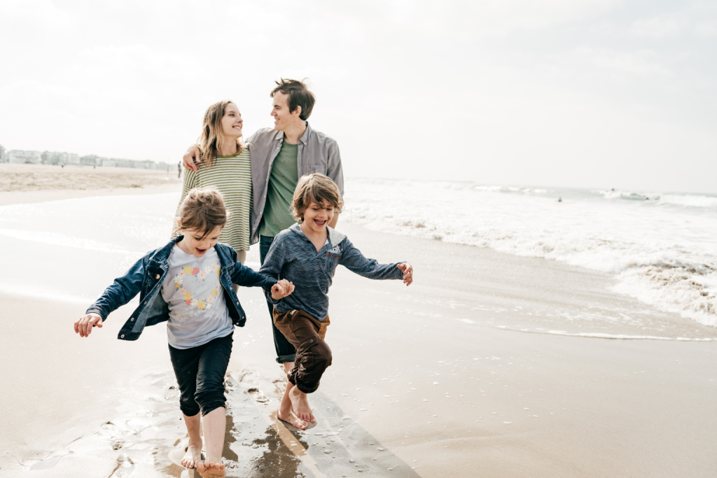 Family with two children walking along the beach shoreline.