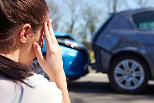 Woman holding her head while looking at two cars involved in a rear-end collision