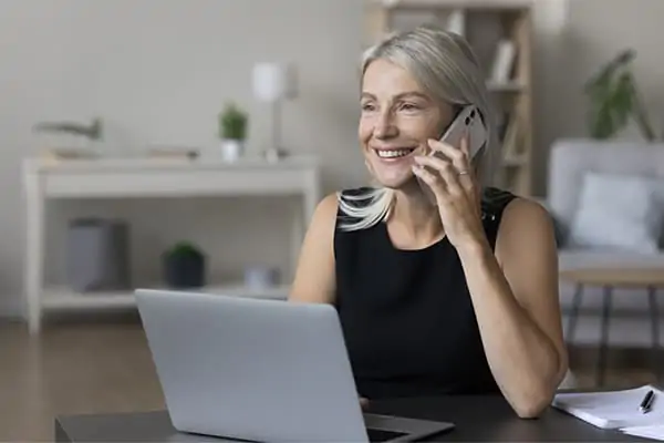 Woman smiling while talking on the phone and working on a laptop at home