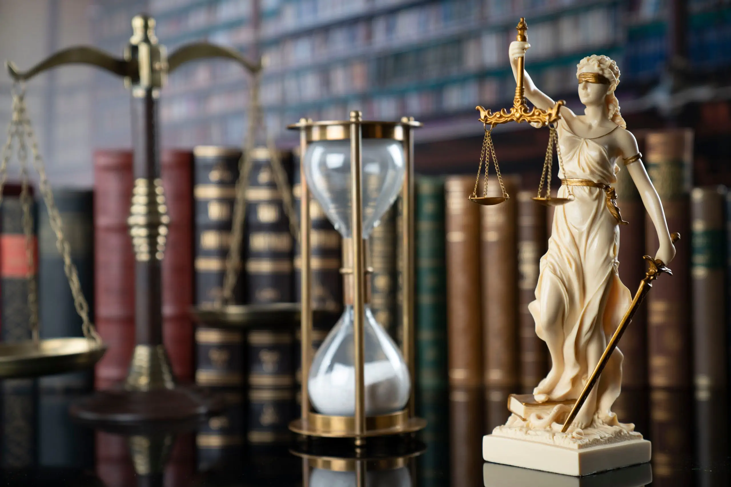 Lady Justice statue with scales and hourglass in front of law books