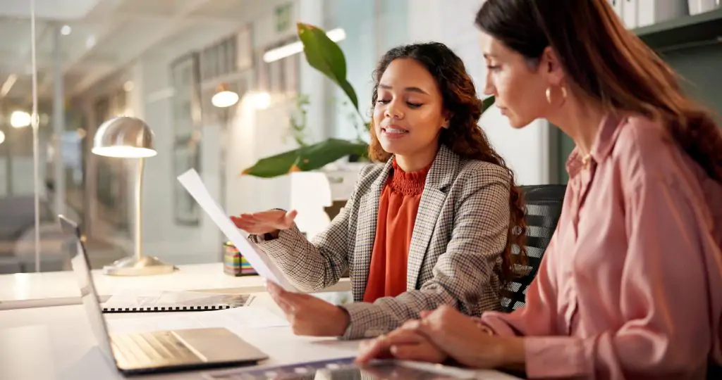 Two women meeting with a professional and reviewing documents at a desk.