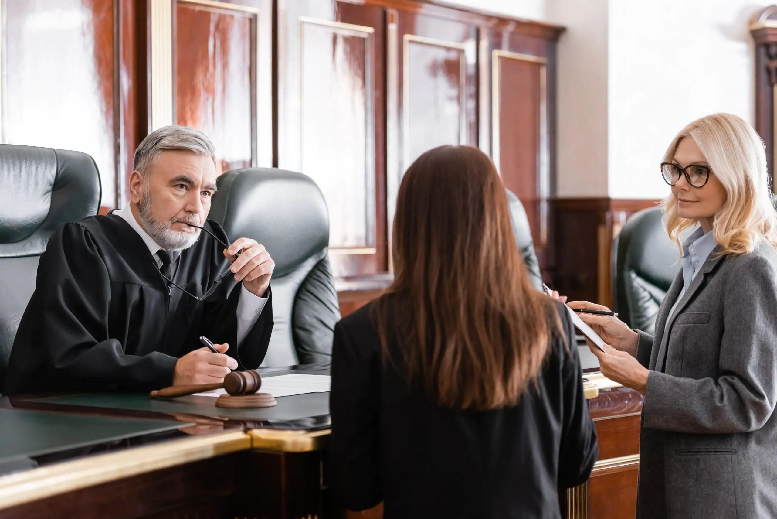 Judge speaking with attorneys and a woman during a courtroom proceeding.