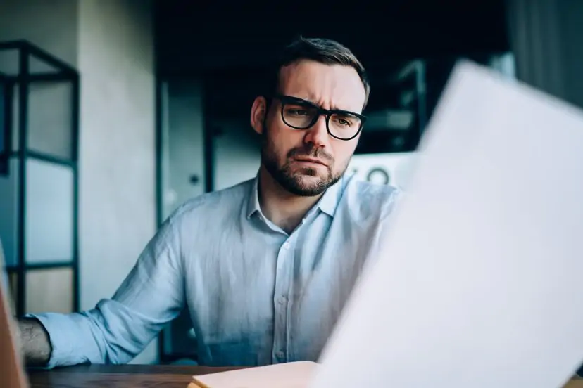 Man reviewing documents on a laptop in an office setting.